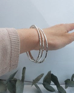 A woman's wrist wearing three silver bangles.